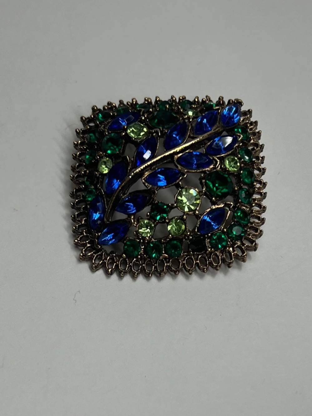 Vintage brooch with blue and green rhinestones arranged in a leaf-like pattern
